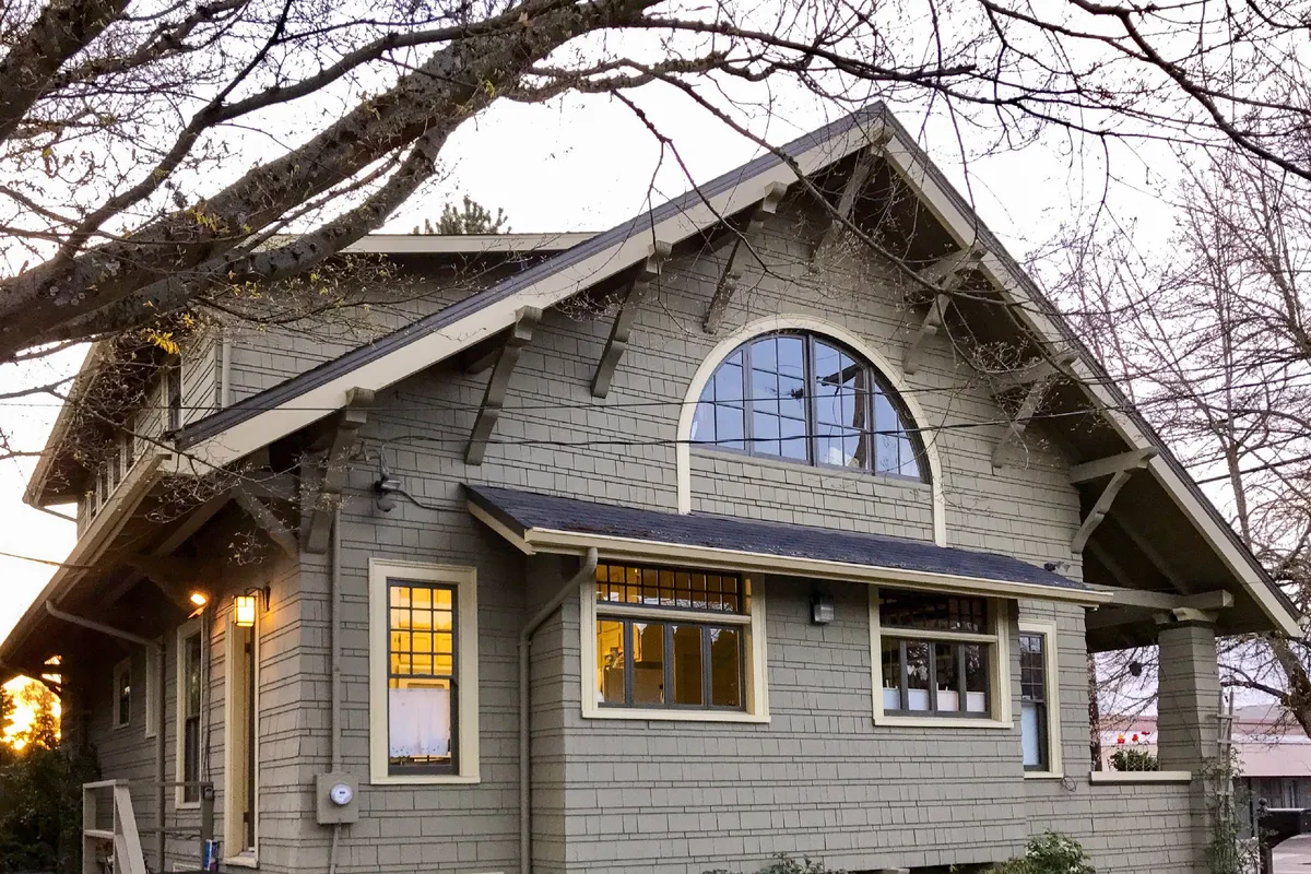 This exterior photo captures the home's front porch with its eye-catching arched window, inviting gable roof, and classic porch columns. The welcoming steps and seating suggest a place where families can gather before heading out to explore downtown.