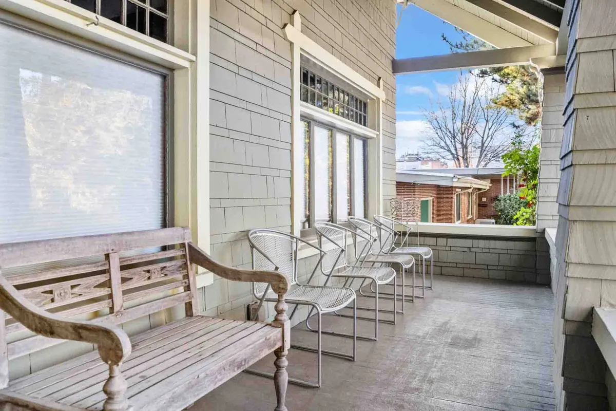 A serene sitting area with a wooden bench and metal chairs set beside large windows, inviting natural light and offering a tranquil spot to relax. The arrangement is conducive to both quiet moments of reflection and lively conversations, echoing the blend of celebration and serenity highlighted in the text.