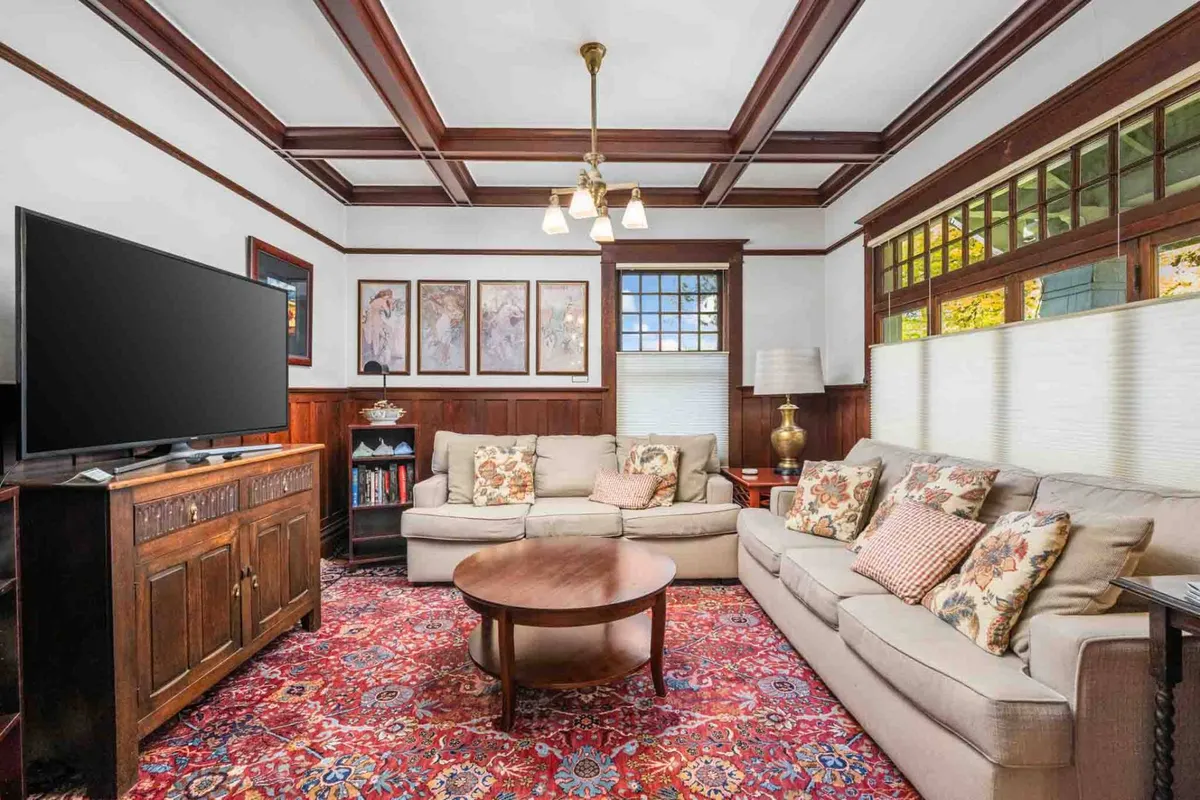 A classic Craftsman living area featuring a plush sofa, artful coffee table, smart TV, tasteful artwork, and a warm lamp. The space blends historic charm with modern convenience, emphasizing comfort and sociability.