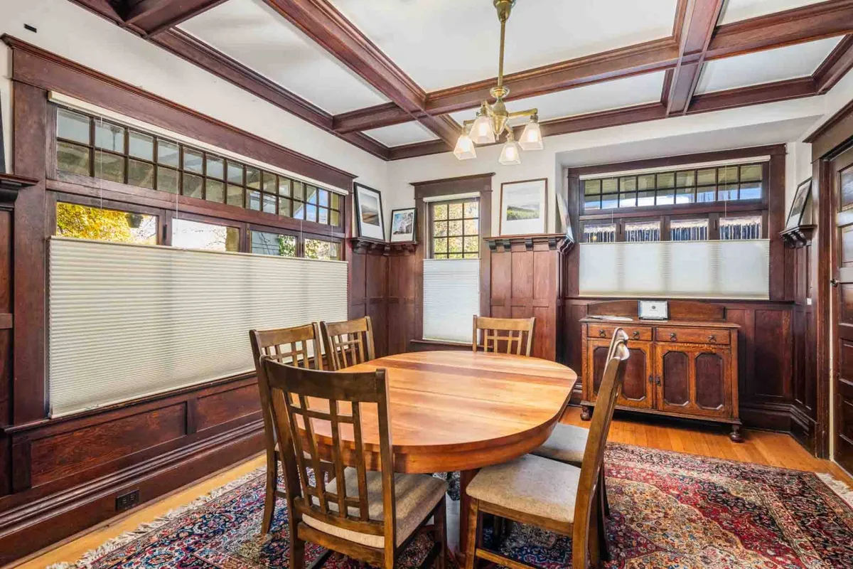 A secondary angle on the dining room, showing a wooden table surrounded by comfortable chairs, a chandelier overhead, wood paneling, and a decorative rug. The setting invites both formal and casual gatherings, adding a sense of warmth and tradition.
