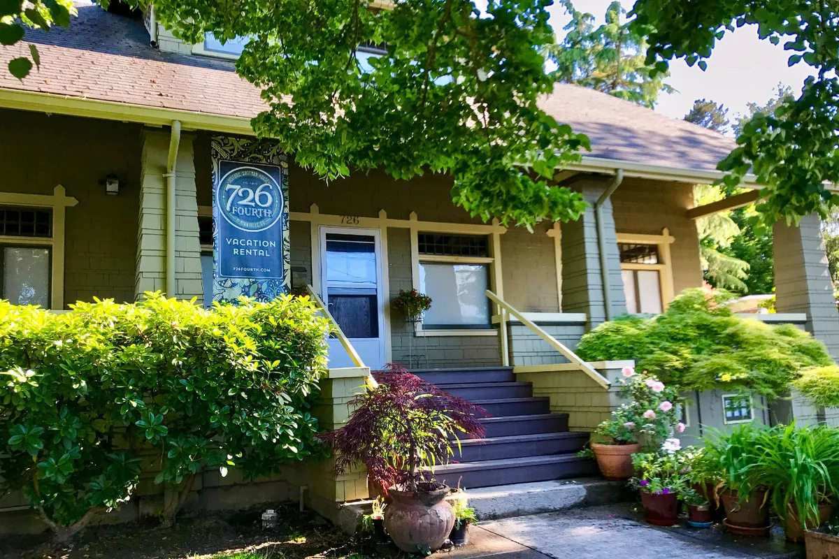 The front entrance of the home, adorned with flower pots and a vacation rental sign, framed by inviting garden greenery. The porch offers a glimpse of relaxing outdoor spaces where guests can unwind.