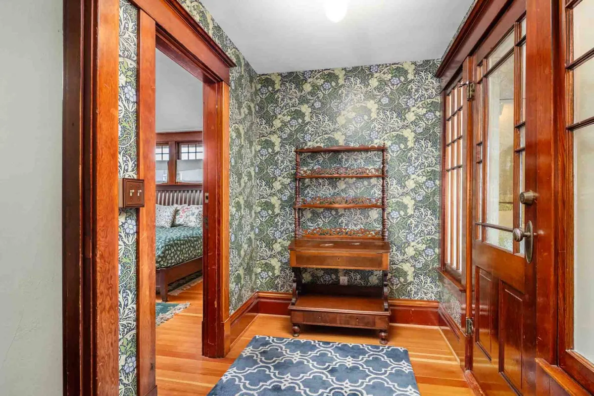 A charming entryway with ornate wallpaper, a wooden shelf, and an intricately framed door, setting a warm and welcoming tone as you step inside the home.