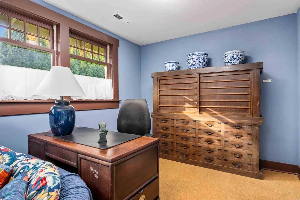 A calm workspace with a desk, blue vase, wooden cabinet, and a lampshade. The area is bright and organized, inviting productivity and focus for work or study.